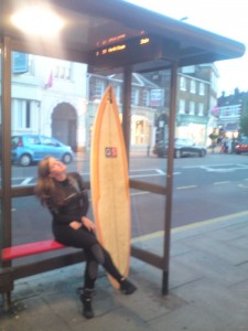 girl with surfboard by bus stop